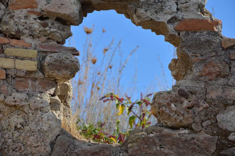 Verlangen naar vrijhedi: zicht op blauwe lucht en een bloeiende plant door gat in een muur